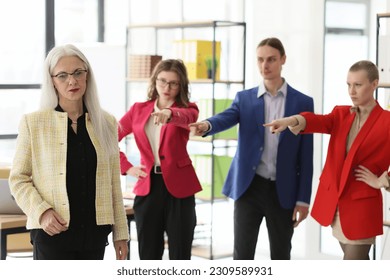 Disappointed employees point fingers to mature staff member standing in company office. Angry colleagues complain on attitude of female worker. Bullying concept
