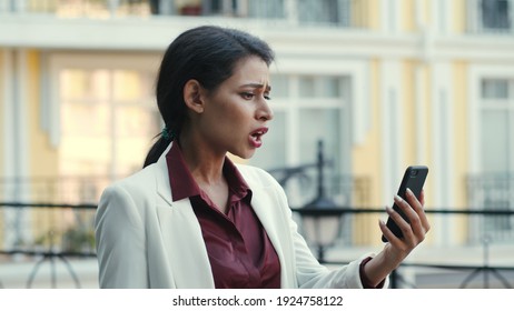 Disappointed Female Entrepreneur Having Video Chat On Mobile Phone At Street. Irritated Businesswoman Discussing Project On Smartphone Outdoors. Sad Mixed Race Woman Looking Phone Screen Outside