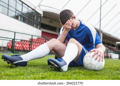 Disappointed football player in blue sitting on pitch after losing on a clear day - Powered by Shutterstock