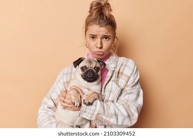 Disappointed frustrated young female pet owner sad because of illness of dog go together to vet clinic dressed in casual clothes isolated over beige background. People animals and care concept