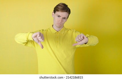 Disappointed Guy Doing Thumbs Down. Yellow Background. 19-20 Years Old Caucasian Guy.