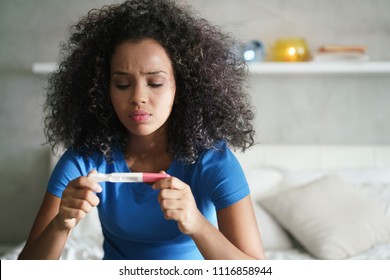 Disappointed Hispanic Girl Getting Unexpected Result From Pregnancy Test Kit. Sad Young Latina Woman Sitting Alone On Her Bed.