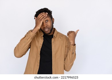 Disappointed Man Pointing With Thumb Aside. Male African American Model In Black T-shirt And Brown Shirt Showing Something, Hand On Forehead. Portrait, Studio Shot, Disappointment Concept