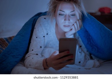 Disappointed sad woman holding mobile phone while lying on bed at night