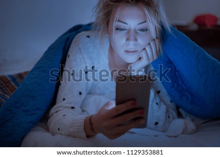 Disappointed sad woman holding mobile phone while lying on bed at night