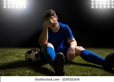 Disappointed soccer player in blue sitting on pitch after losing the match - Powered by Shutterstock