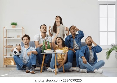 Disappointed sports fans watching letdown match on TV. Frustrated young men and women sitting on sofa at home and drinking beer. Upset friends frustrated with lost soccer game