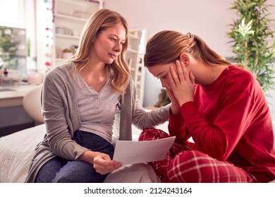 Disappointed Teenage Daughter Wearing Pyjamas Looking At School Exam Report With Mother In Bedroom