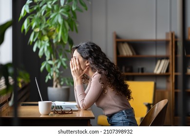Disappointed woman office worker struggling through task, being unproductive, tired overworked female employee covering face with hands and thinking about solution while sitting at table with laptop