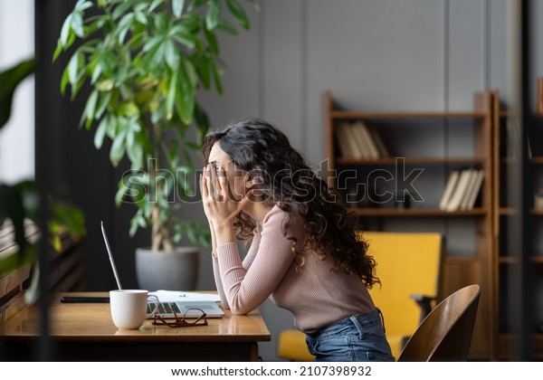 Disappointed woman office worker struggling\
through task, being unproductive, tired overworked female employee\
covering face with hands and thinking about solution while sitting\
at table with\
laptop
