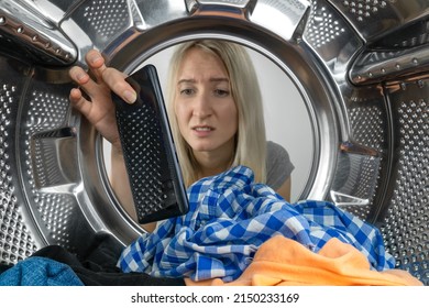 Disappointed young blonde woman finds her mobile phone in the washing machine after washing clothes, photo from inside