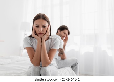 Disappointed young caucasian lady sits on bed, ignores offended man. Frustrated sad wife sit on bed thinking about relationship problems, thoughtful couple after quarrel, upset lovers consider parting