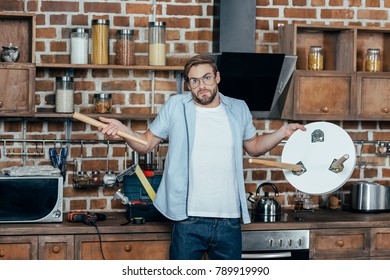 disappointed young man in eyeglasses holding broken stool and looking at camera
