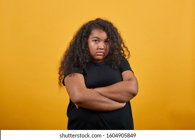 Disappointed young woman with overweight keeping hands crossed, looking at camera over isolated orange background wearing fashion black shirt. People lifestyle concepte.