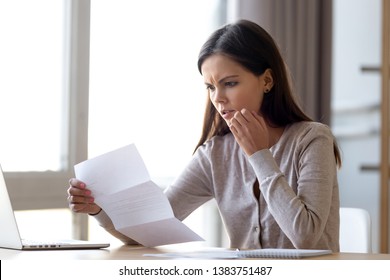 Disappointed young woman sit on table at home read bad news eviction notice in paperwork letter, shocked female surprised by unpleasant message warning notification received in paper mail