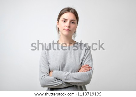 Disappointment, confusion, bad mood. Frustrated young woman with crossed hands stands isolated on white.