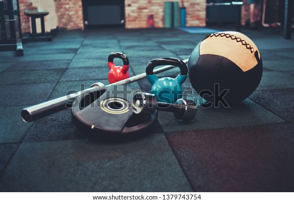 Disassembled barbell, medicine ball, kettlebell,\
dumbbell lying on floor in gym. Sports equipment for workout with\
free weight. Functional\
training