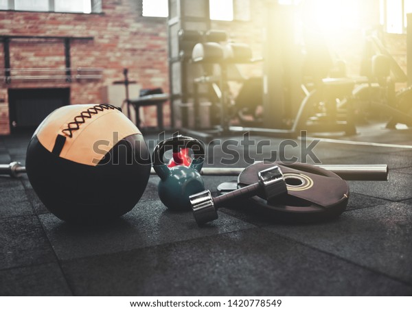 Disassembled barbell, medicine ball, kettlebell,\
dumbbell lying on floor in gym. Sports equipment for workout with\
free weight. Functional\
training