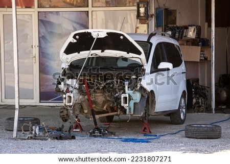 Disassembled car without bumper, without engine with open hood on jack without front wheels. Total repair after a hard accident, parts replacement