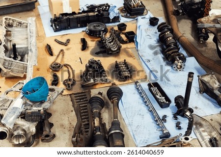 Disassembled engine components spread across workshop floor showing crankshaft, driveshaft, chains, housing and tools. Vehicle check-up and repair. Underbody chassis and suspension parts