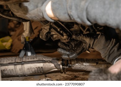 Disassembly and renovation of a car's steering system in the workshop. The power steering oil is dripping onto the mechanic's hands. Tail-pipe or exhaust tube on the ground. - Powered by Shutterstock