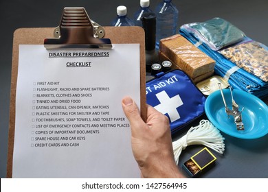 Disaster preparedness checklist on a clipboard with disaster relief items in the background.Such items would include a first aid kit,flashlight,tinned food,water,batteries and shelter.