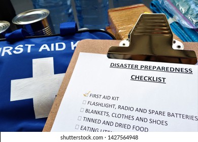 Disaster preparedness checklist on a clipboard with disaster relief items in the background.Such items would include a first aid kit,flashlight,tinned food,water,batteries and shelter.Be prepared.