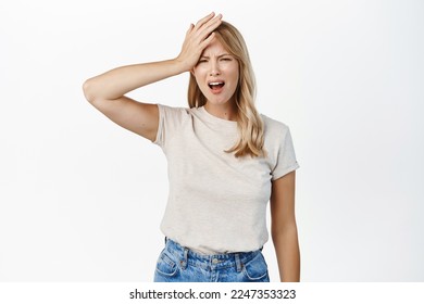 Disaster. Troubled blond girl holding hand on head and grimacing, feeling disappointed, upset by smth, standing over white background - Shutterstock ID 2247353323