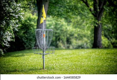 A disc golf hole on green grass with the woods in background.