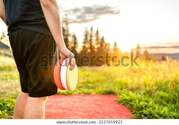 Disc golf in summer at sunset. Man with\
equipment in park course. Guy playing discgolf. Player in outdoor\
sport tournament. Landscape in\
Finland.