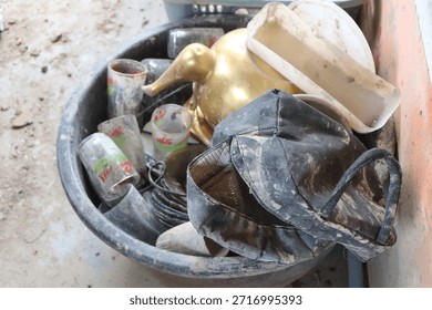 Discarded and dirty objects like a bag, glasses, and a golden kettle are piled in a tub, covered in mud