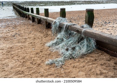 A  Discarded Fisherman's Net With Ropes Caught In The Wooden Sea Breakwater On A Sandy Beack On The South Coast Of England, UK. Hazardous To Marine Life.