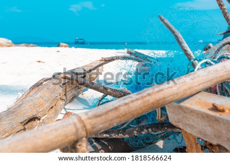 Discarded Fishing Net tangled on a tropical beach. Turquoise plastic mesh fishnet entangled with driftwood litter & debris. Litter polluting beaches, environmental issue, ocean trash. Colourful scene.