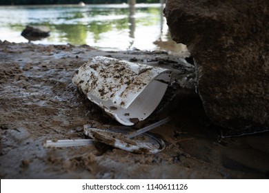 Discarded Food Containers Litter The Area Under A Bridge Near A River With Trash That Includes Plastic Straws, Plastic Lids, A Styrofoam Cup And Other Plastic Food Waste, Contributing To Pollution.