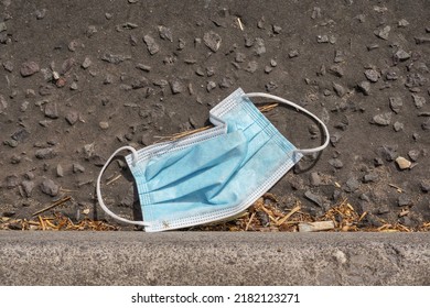 Discarded medical face mask on road next to curb. Pandemic pollution. Used face mask thrown away on street 