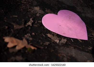 Discarded Pink Construction Paper Heart On The Ground, With A Narrow Depth Of Field, Highlighting The Tire Tracks  That Cross Its Face. 