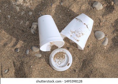 discarded plastic coffee cups and lis lying in the sand