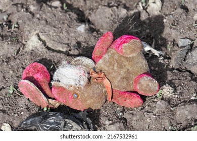 Discarded torn child plush toy, pink bunny in the mud. Lost rabbit, abandoned bunny doll