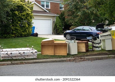 Discarded wooden furniture and an old bed lined up by the curb near a street waiting for trash pickup - Shutterstock ID 2091522364