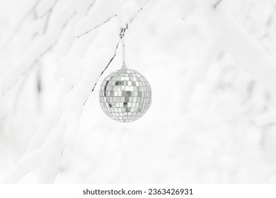 A disco ball hanging on a snowy tree branch - Shutterstock ID 2363426931