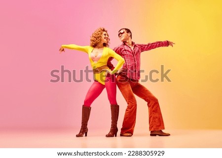 Disco dance. Stylish expressive excited couple of professional dancers in retro style clothes dancing over pink-yellow background. Concept of 70s, 80s fashion style, music and emotions