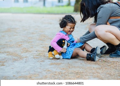 Disconsolate Hispanic Toddler Girl Three Years Old Crying While Sit On The Ground Outdoor. Her Ecuadorian Mother Try To Calm Down On The City Street.