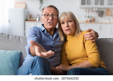 Discontented Senior Couple Talking To Camera Disapproving Criticizing Something Sitting Together On Sofa At Home. Displeased Customers. Communication Problems With Older Parents