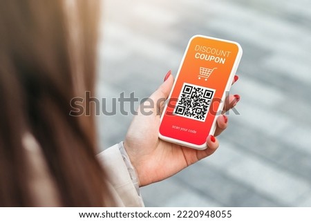 Discount coupon with QR code on smartphone in a female hand on a green grass background. copy space