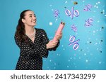 Discount offer. Happy young woman blowing up party popper on light blue background. Confetti and percent signs in air