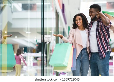 Discount Prices. Smiling Black Couple Shopping In Mall Together, Looking At Showcase With Interest, African Spouses Walking In Department Store With Bright Shopper Bags, Enjoying Seasonal Sales