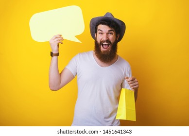 Discounts concept, shopping time, happy bearded guy wearing a hat, holding a small bag and a empty speach bubble - Shutterstock ID 1451641343