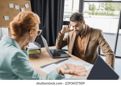 discouraged manager looking at papers near blurred businesswoman gesturing during conflict in office - Powered by Shutterstock