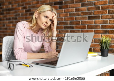 Discouraged middle-aged woman sitting at the laptop,does not know what to do,at office,looking at laptop screen,worried and tired, an entrepreneur woman is thinking how to save business in the crisis