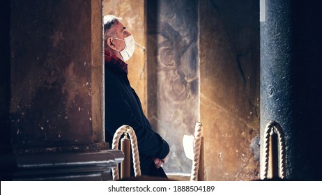 A Discouraged Priest is Praying in an Empty Church, Wearing a Face Mask During Covid-19 Pandemic. Churches Are Being Visited Less Frequently by the Faithful Due to Coronavirus Spread Concerns 